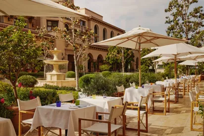 The Terrace outdoor dining beside a tiered stone fountain, white umbrellas and manicured garden.