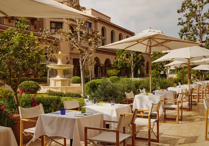 The Terrace outdoor dining beside a tiered stone fountain, white umbrellas and manicured garden.