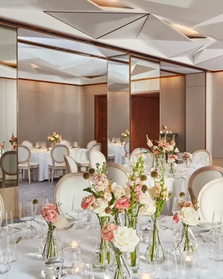 Round tables with white chairs, floral centrepieces, and mirrored walls reflecting soft daylight.