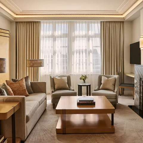 Spacious living room with sofa and armchairs, central coffee table, large window with curtains, and a marble fireplace with mirror.