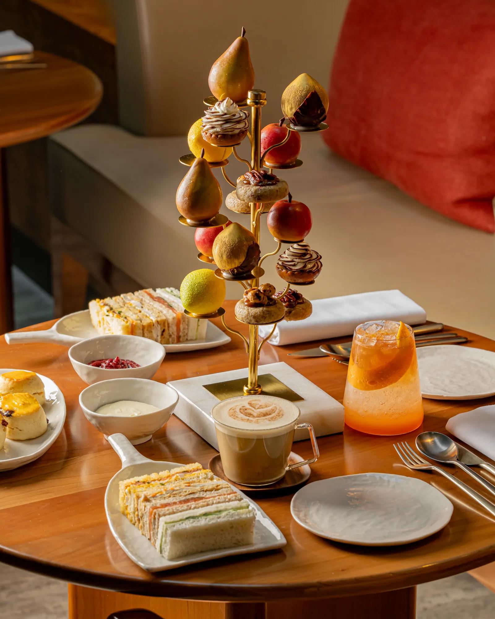 Elegant afternoon tea display featuring finger sandwiches, pastries, fresh fruit and coffee served on a tiered stand in a stylish lounge setting.