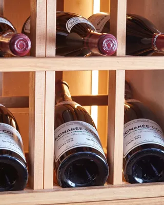 Red wine bottles stored horizontally in a wooden rack, with labels and corks visible under warm lighting.