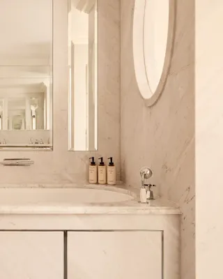 Elegant marble bathroom featuring a built-in bathtub beneath large mirrors, chrome fixtures, and a heated towel rail, with toiletries neatly arranged along the edge.