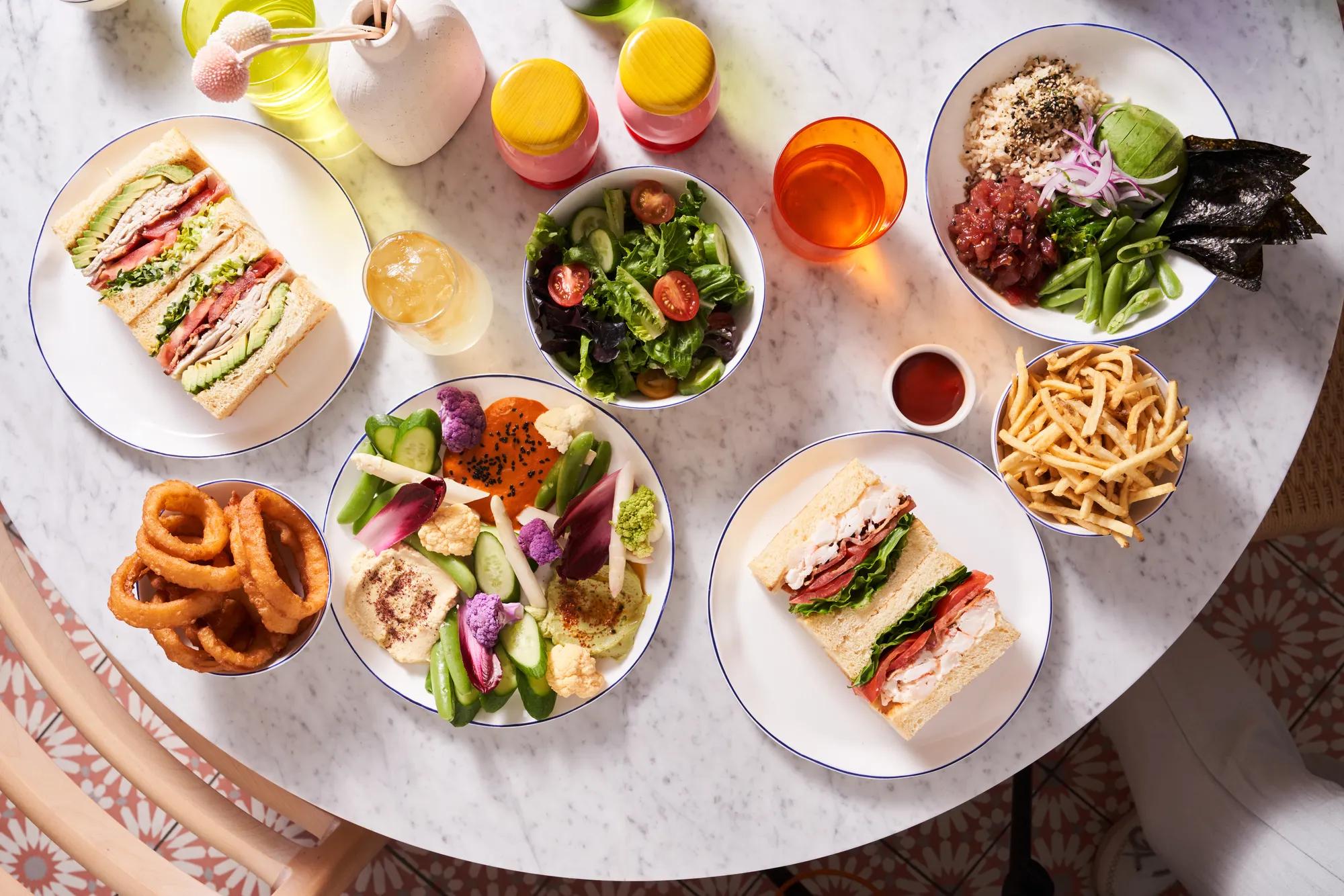 Table with sandwiches, salad, fries, onion rings, and colorful vegetable platter