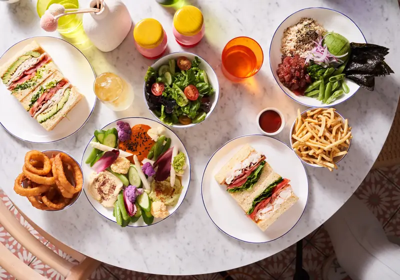 Table with sandwiches, salad, fries, onion rings, and colorful vegetable platter