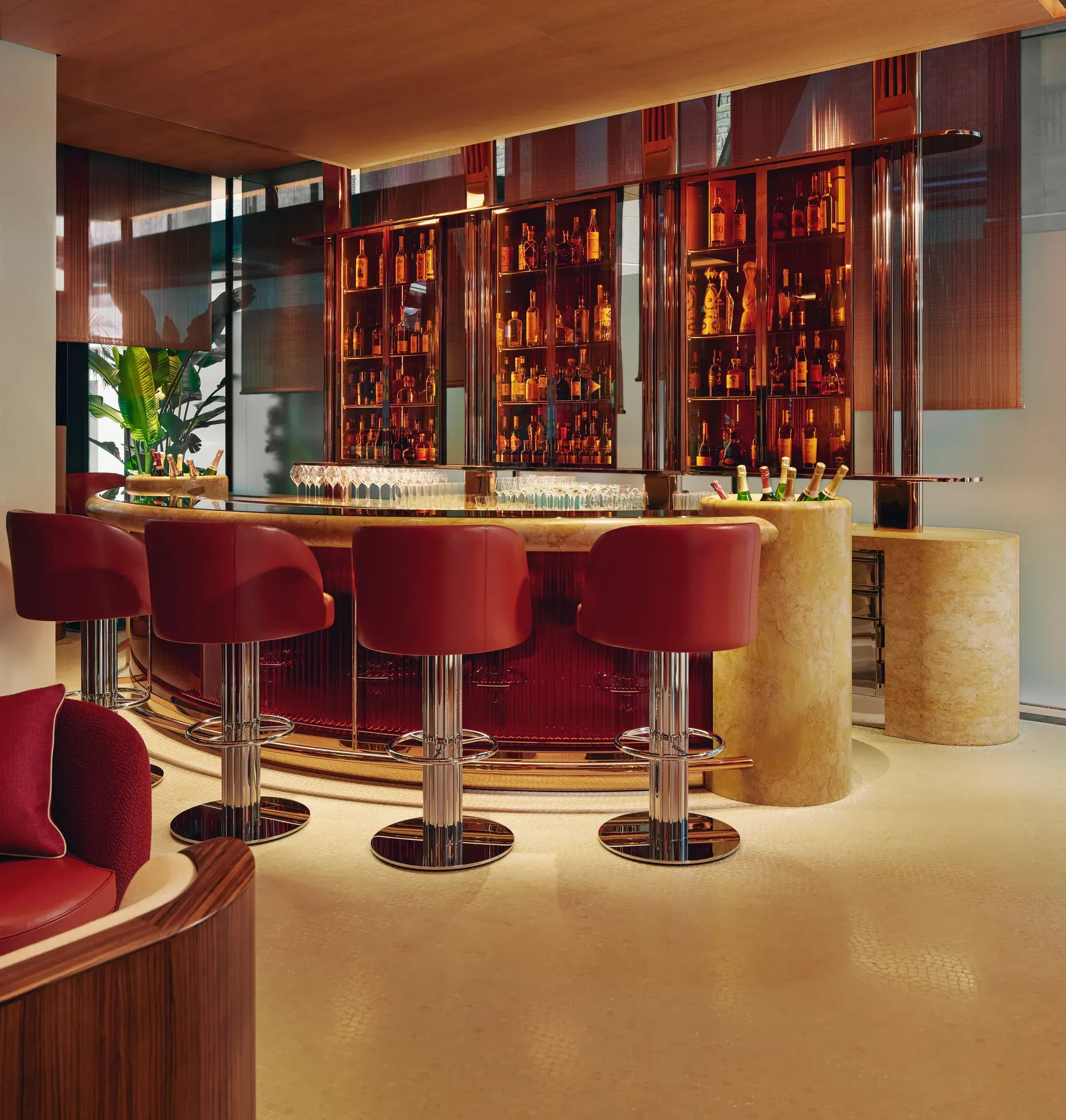 Curved bar with red leather stools, backlit orange bottle display, and polished chrome finishes in a modern hotel.