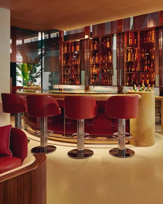 Curved bar with red leather stools, backlit orange bottle display, and polished chrome finishes in a modern hotel.