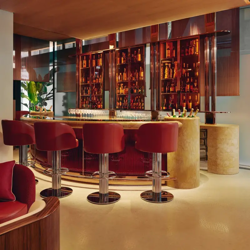 Curved bar with red leather stools, backlit orange bottle display, and polished chrome finishes in a modern hotel.