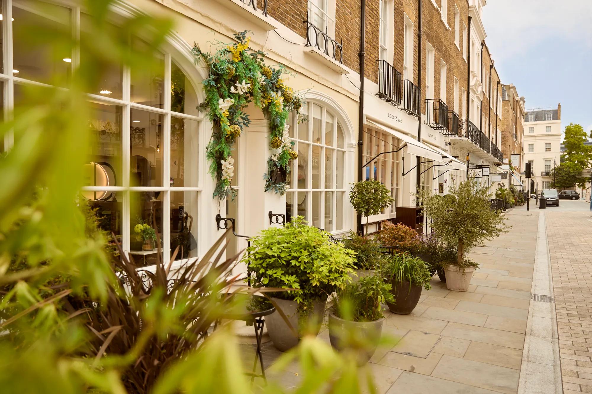 Elegant boutique storefront with floral display, large windows, and potted plants along a quiet residential-style street.