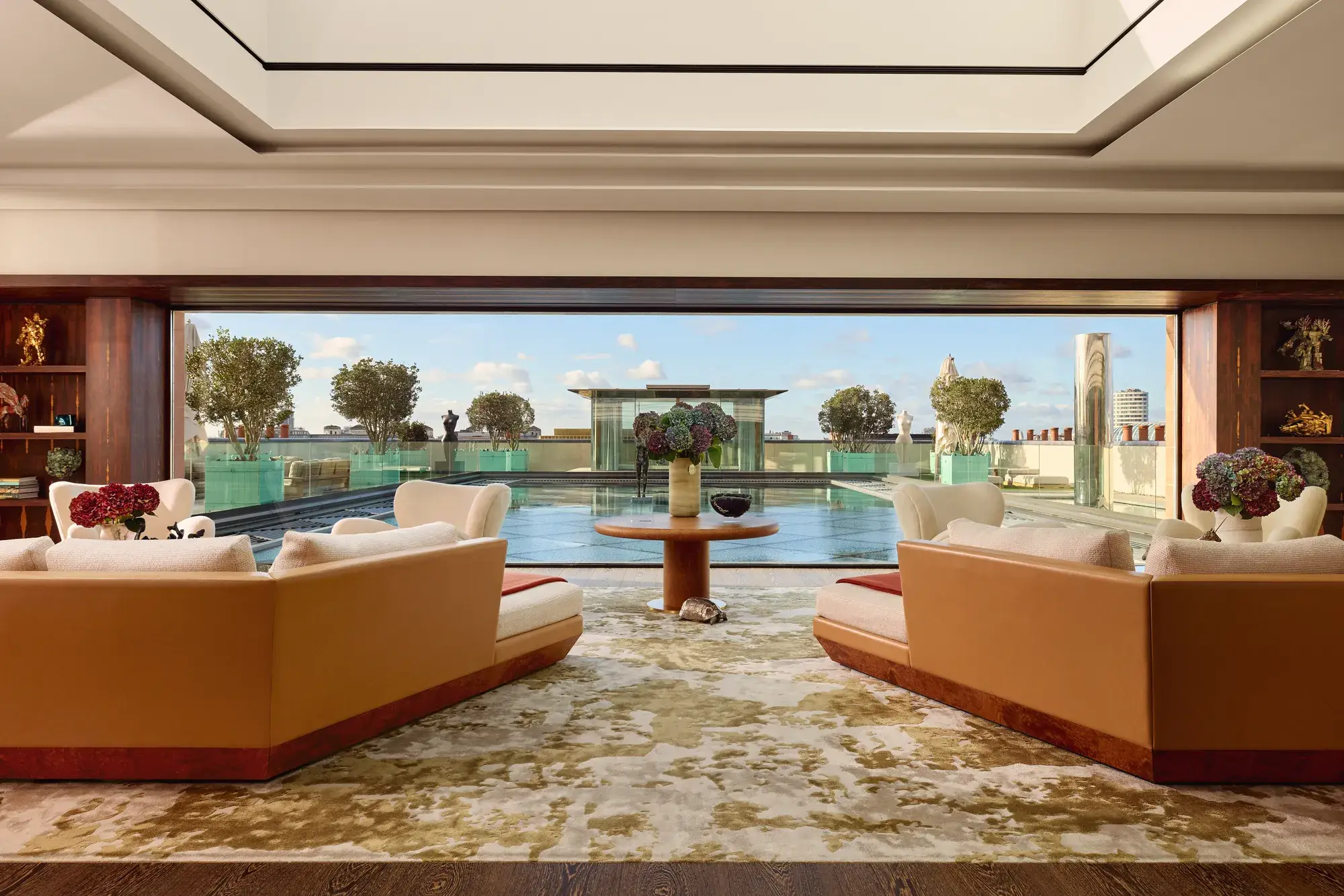 Spacious penthouse living room at Claridge’s with large sofas facing a glass wall opening onto a rooftop terrace and reflective pool.