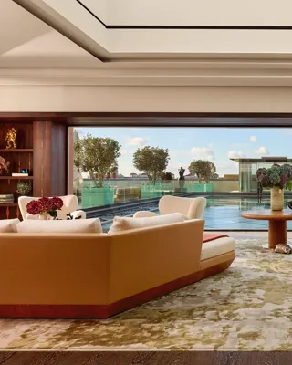 Spacious penthouse living room at Claridge’s with large sofas facing a glass wall opening onto a rooftop terrace and reflective pool.