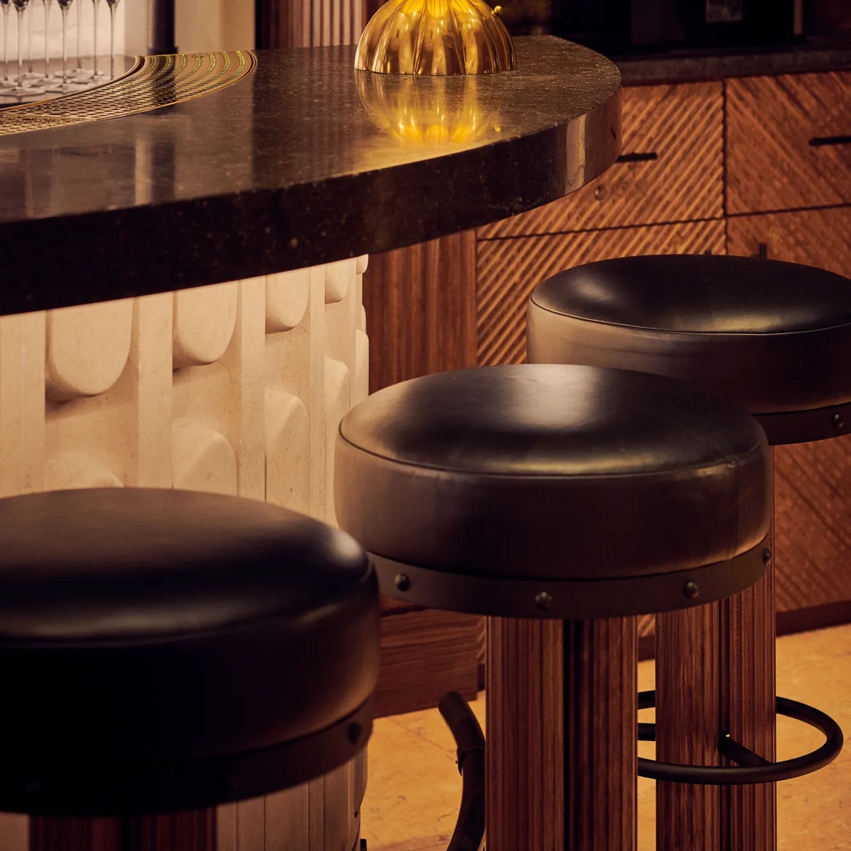 Close-up of bar counter with golden globe lamp and leather bar stools in warm lighting.