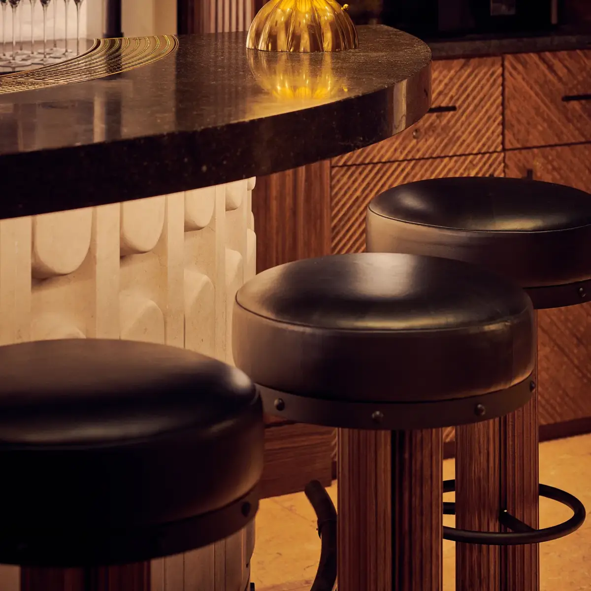Close-up of bar counter with golden globe lamp and leather bar stools in warm lighting.
