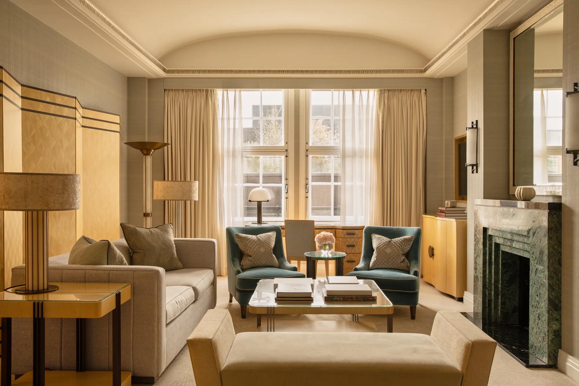 Contemporary living room with a sofa, armchairs and coffee table, centred around a green marble fireplace and framed by tall windows with sheer curtains.