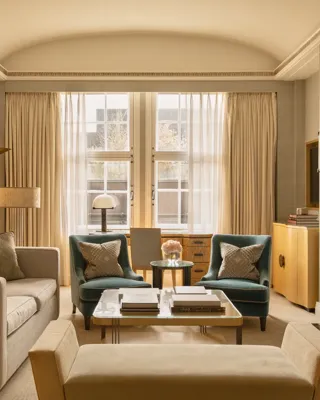 Contemporary living room with a sofa, armchairs and coffee table, centred around a green marble fireplace and framed by tall windows with sheer curtains.