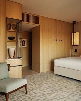 Hotel bedroom with a large bed, soft patterned carpet, light wood panelled walls, and a green upholstered chair in the foreground.