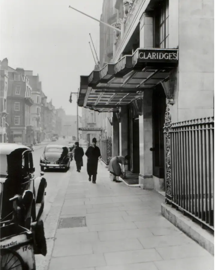 Historic black-and-white view of Claridge’s entrance with vintage cars and pedestrians on Brook Street.