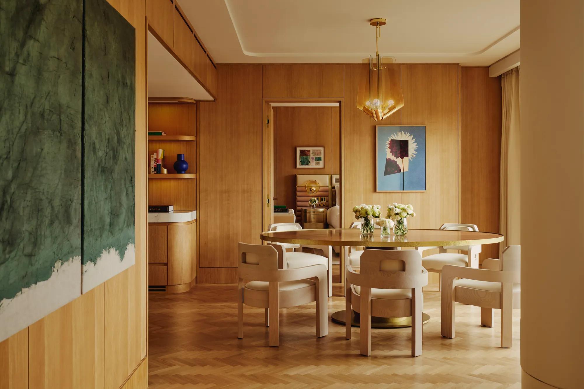 Dining table set for six with floral centrepieces, natural wood finishes and park views through a floor-to-ceiling window.
