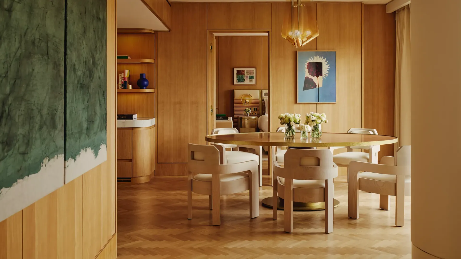 Dining table set for six with floral centrepieces, natural wood finishes and park views through a floor-to-ceiling window.