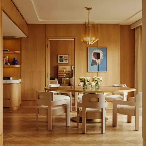 Dining table set for six with floral centrepieces, natural wood finishes and park views through a floor-to-ceiling window.