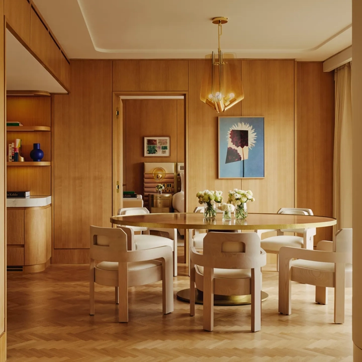 Dining table set for six with floral centrepieces, natural wood finishes and park views through a floor-to-ceiling window.