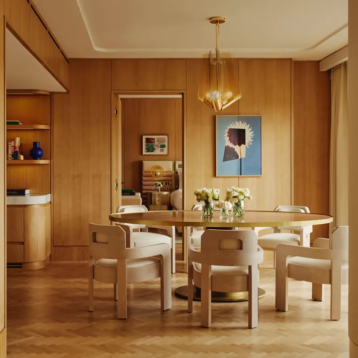 Dining table set for six with floral centrepieces, natural wood finishes and park views through a floor-to-ceiling window.