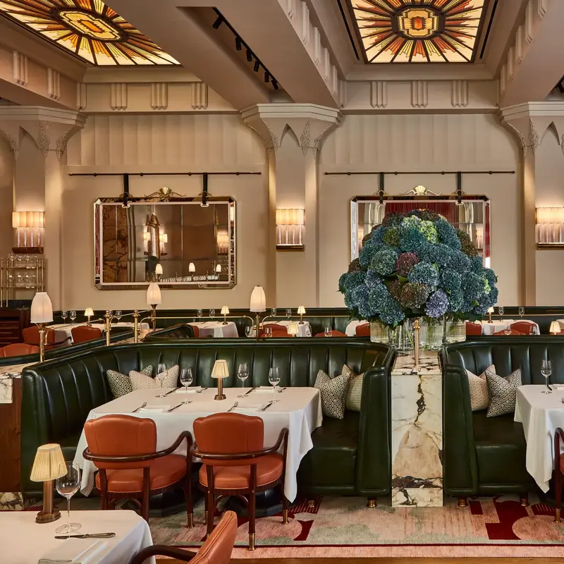 Elegant restaurant with green leather banquettes, art deco ceiling, and a large hydrangea floral centrepiece.