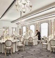 Elegant ballroom at Claridge’s set for a wedding reception, featuring round tables with white floral centrepieces, chandeliers, and mirrored accents in a refined Art Deco design.
