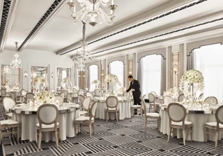 Elegant ballroom at Claridge’s set for a wedding reception, featuring round tables with white floral centrepieces, chandeliers, and mirrored accents in a refined Art Deco design.