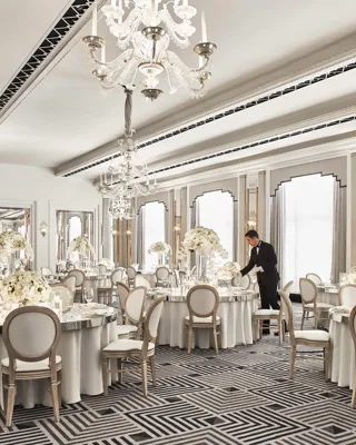 Elegant ballroom at Claridge’s set for a wedding reception, featuring round tables with white floral centrepieces, chandeliers, and mirrored accents in a refined Art Deco design.