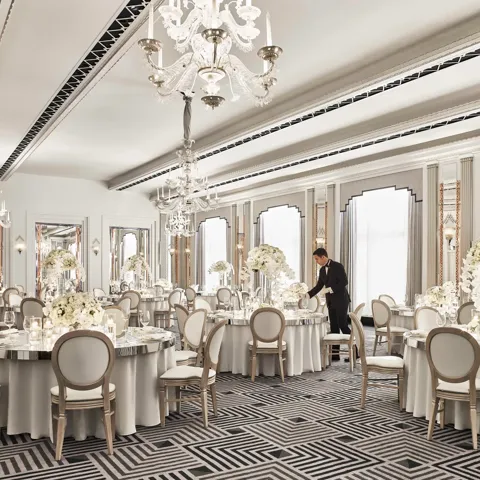 Elegant ballroom at Claridge’s set for a wedding reception, featuring round tables with white floral centrepieces, chandeliers, and mirrored accents in a refined Art Deco design.