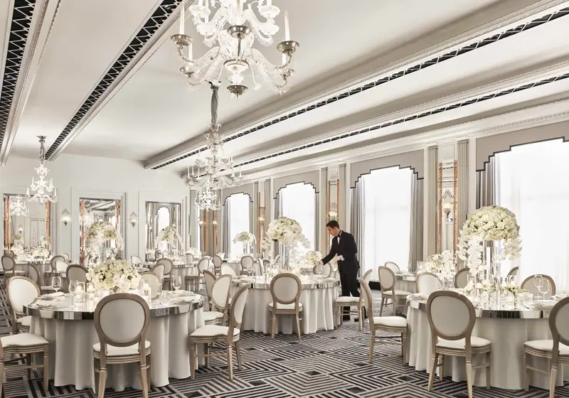Elegant ballroom at Claridge’s set for a wedding reception, featuring round tables with white floral centrepieces, chandeliers, and mirrored accents in a refined Art Deco design.