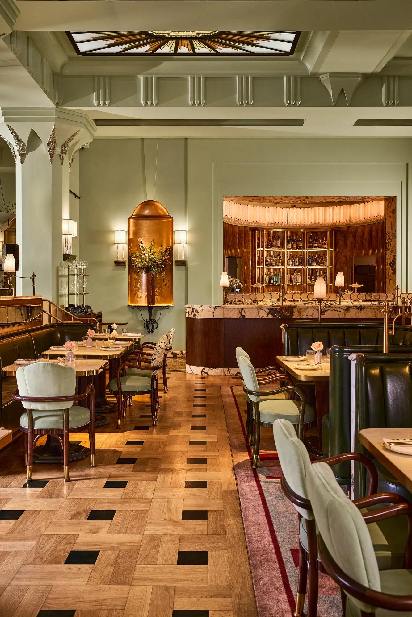 Elegant restaurant dining room with tables, upholstered seating, and a softly lit bar in the background.
