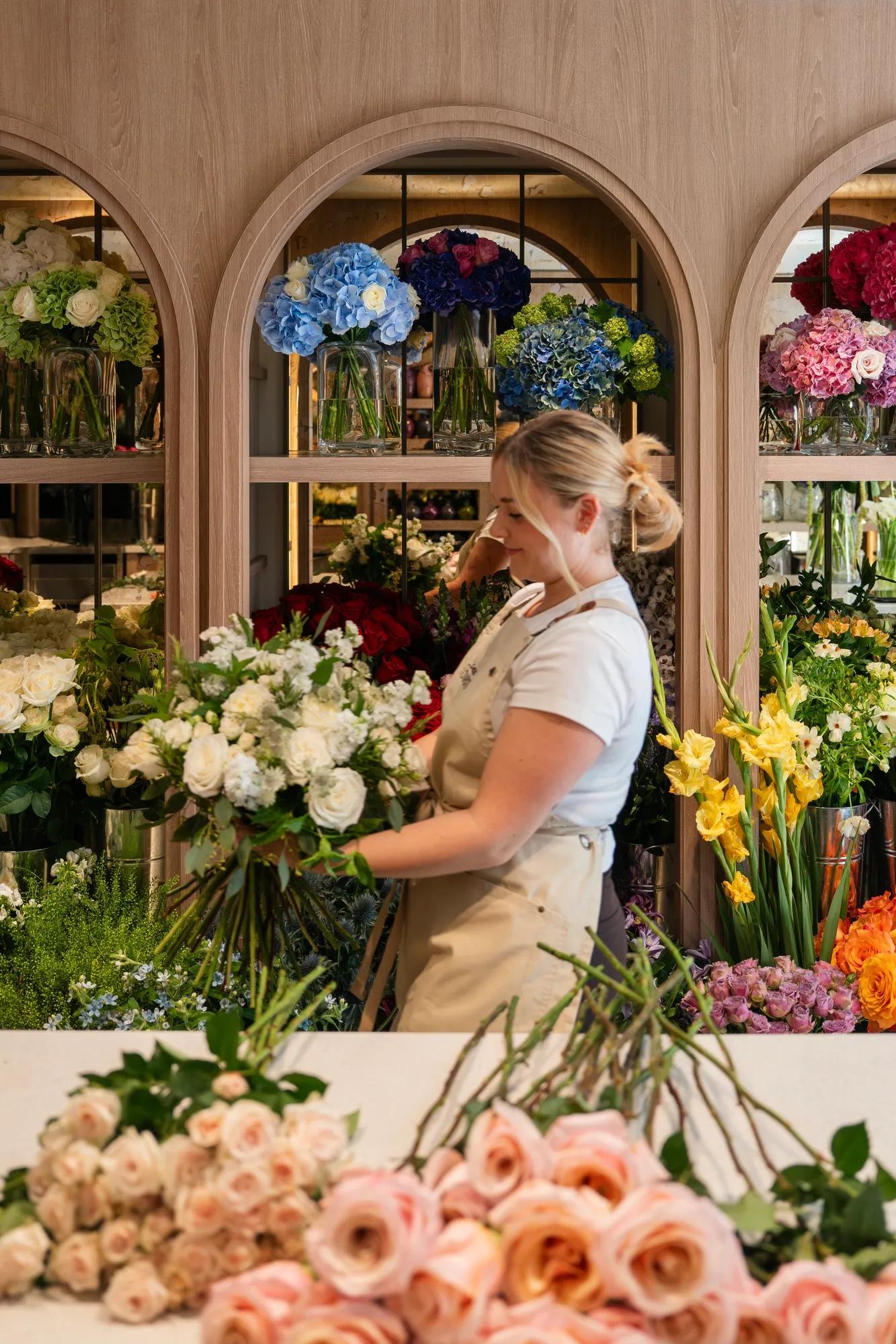 Florist arranging a bouquet surrounded by colourful seasonal flowers inside Claridge’s Flowers.