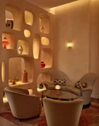 Cozy lounge corner with curved armchairs, sculptural shelving, and warm ambient lighting.