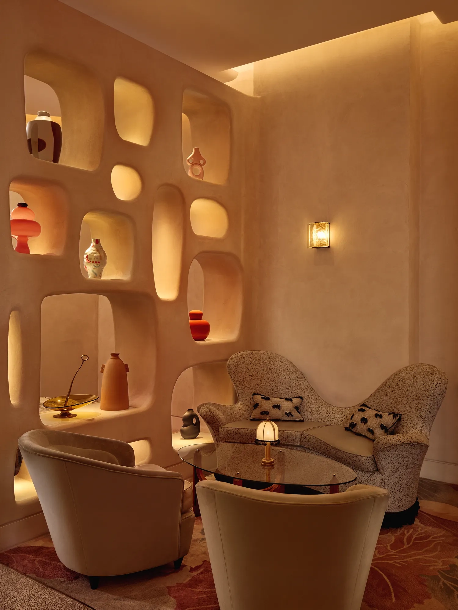 Cozy lounge corner with curved armchairs, sculptural shelving, and warm ambient lighting.