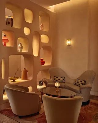 Cozy lounge corner with curved armchairs, sculptural shelving, and warm ambient lighting.