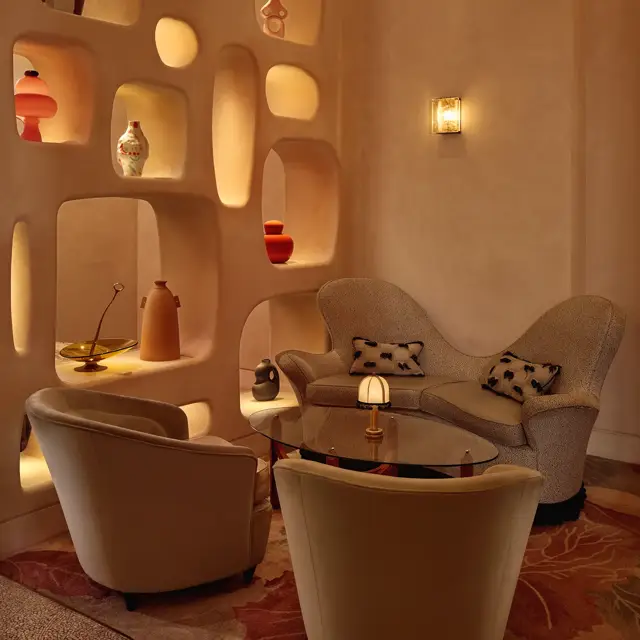 Cozy lounge corner with curved armchairs, sculptural shelving, and warm ambient lighting.