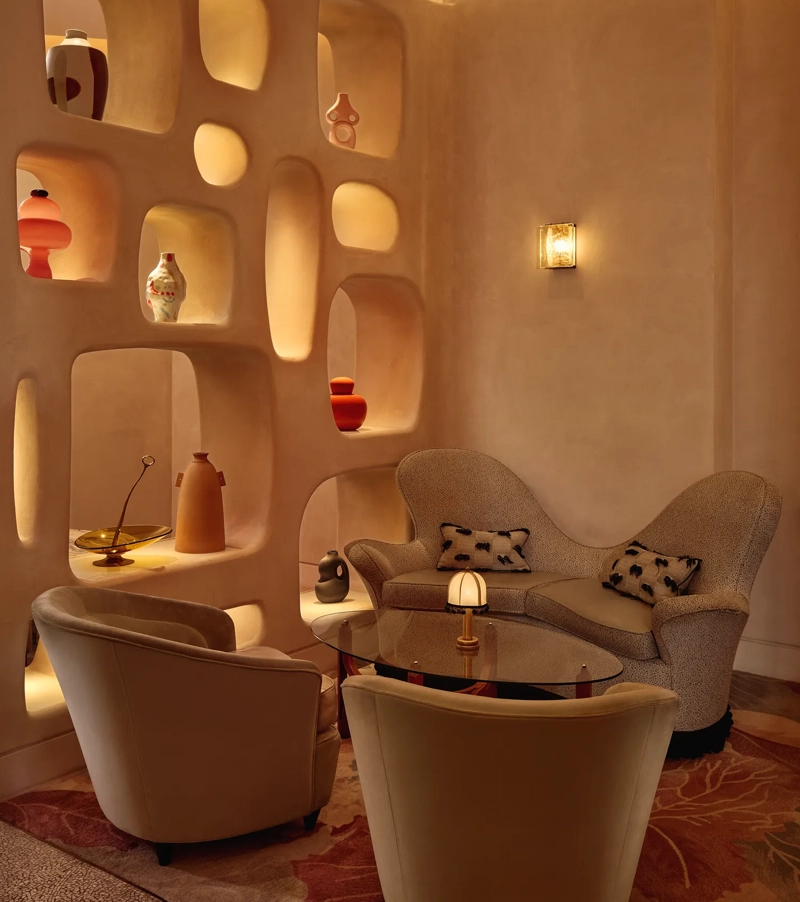 Cozy lounge corner with curved armchairs, sculptural shelving, and warm ambient lighting.