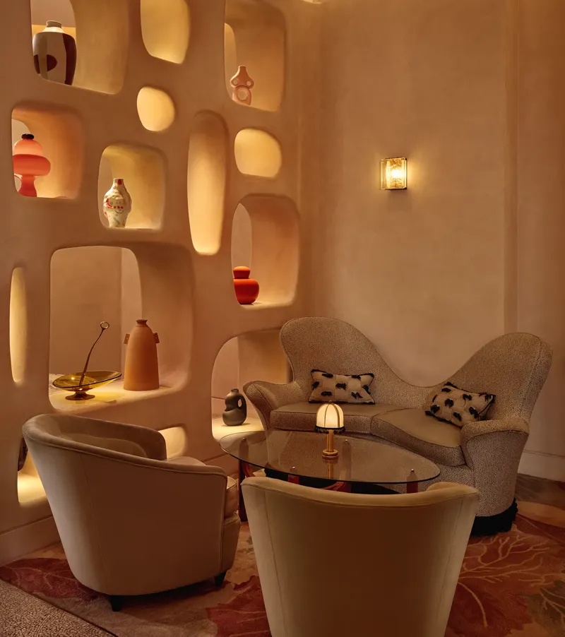 Cozy lounge corner with curved armchairs, sculptural shelving, and warm ambient lighting.