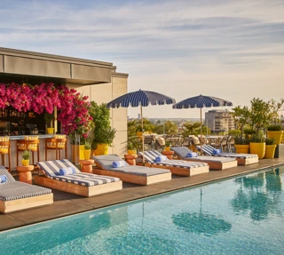 Rooftop pool with striped loungers, blue parasols and a flower-covered bar overlooking the city skyline.