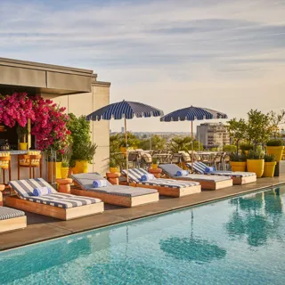 Rooftop pool with striped loungers, blue parasols and a flower-covered bar overlooking the city skyline.