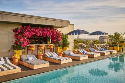 Rooftop pool with striped loungers, blue parasols and a flower-covered bar overlooking the city skyline.