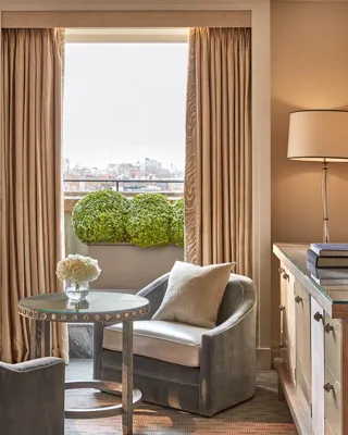 Seating area with two grey armchairs, round table, and balcony view framed by tall curtains.
