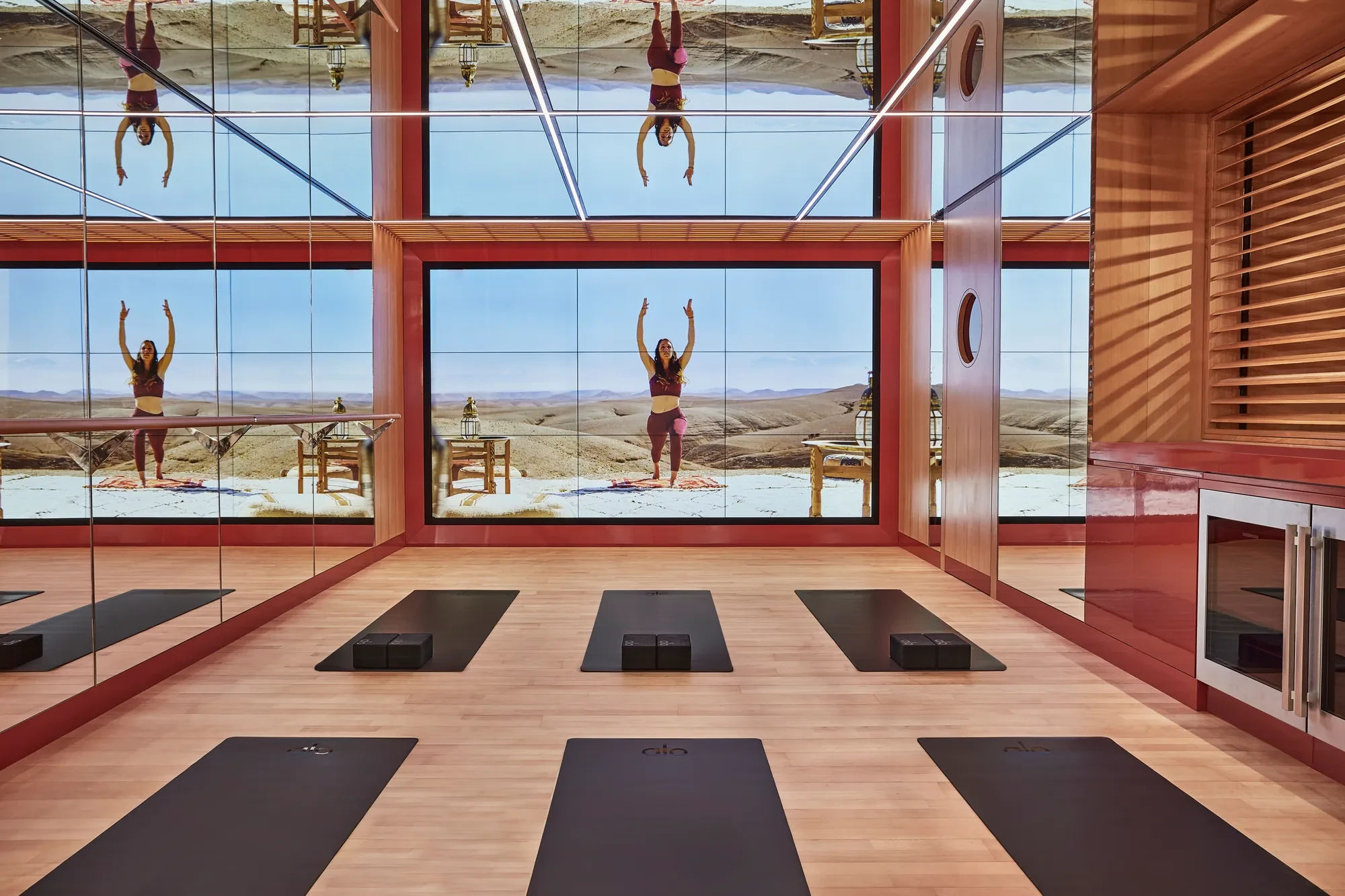 Modern yoga studio with mirrored walls, virtual instructor screen, and black yoga mats.