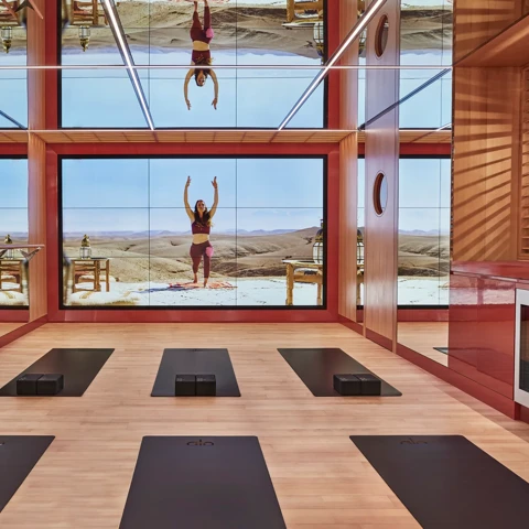 Modern yoga studio with mirrored walls, virtual instructor screen, and black yoga mats.