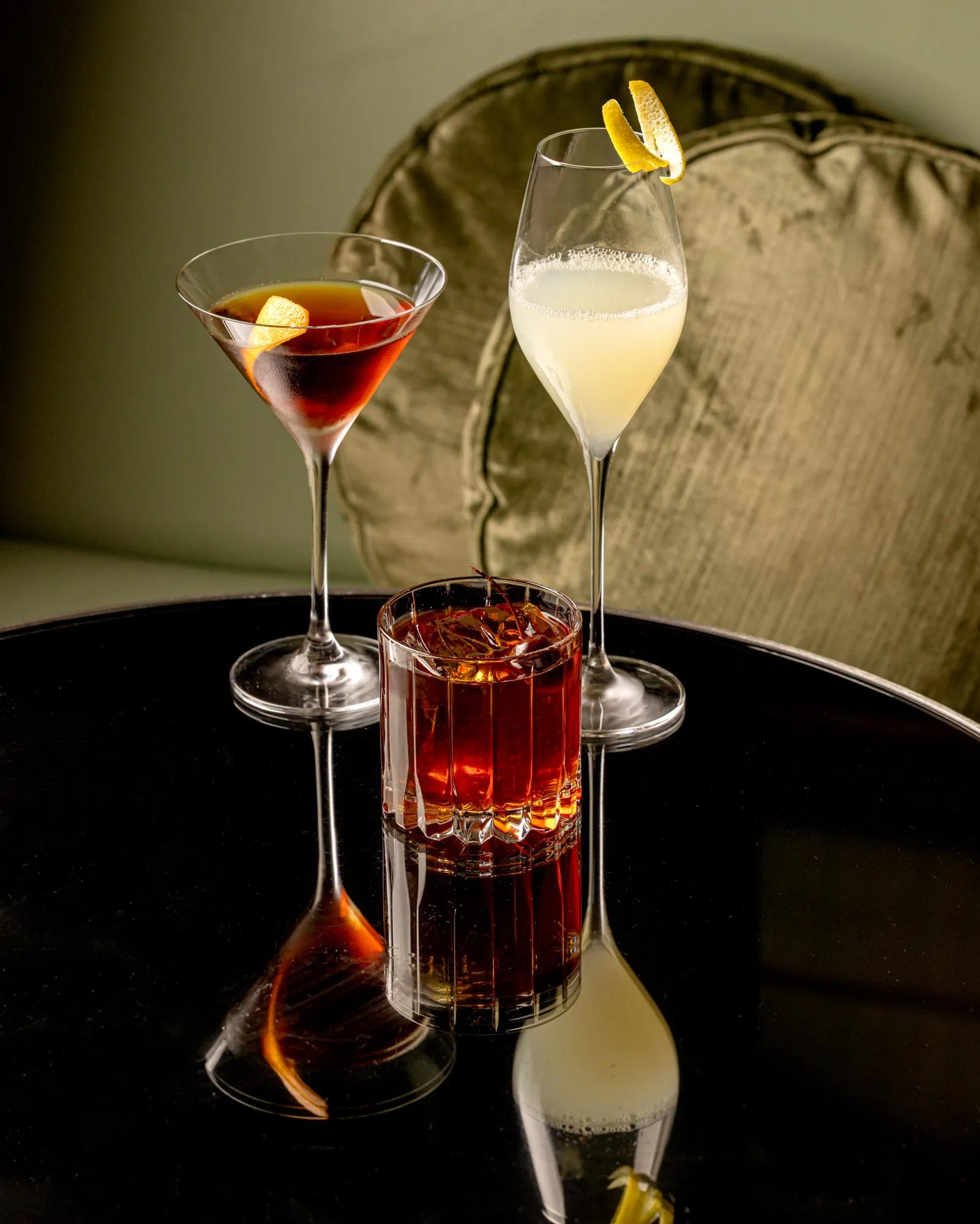 Three drinks arranged on a table, each in a different glass with distinct colors and garnishes.