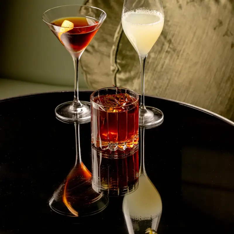 Three drinks arranged on a table, each in a different glass with distinct colors and garnishes.