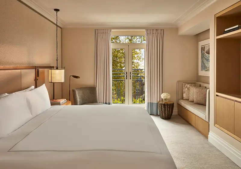 Hotel room with king bed, soft neutral tones, French doors to balcony, and seating area.