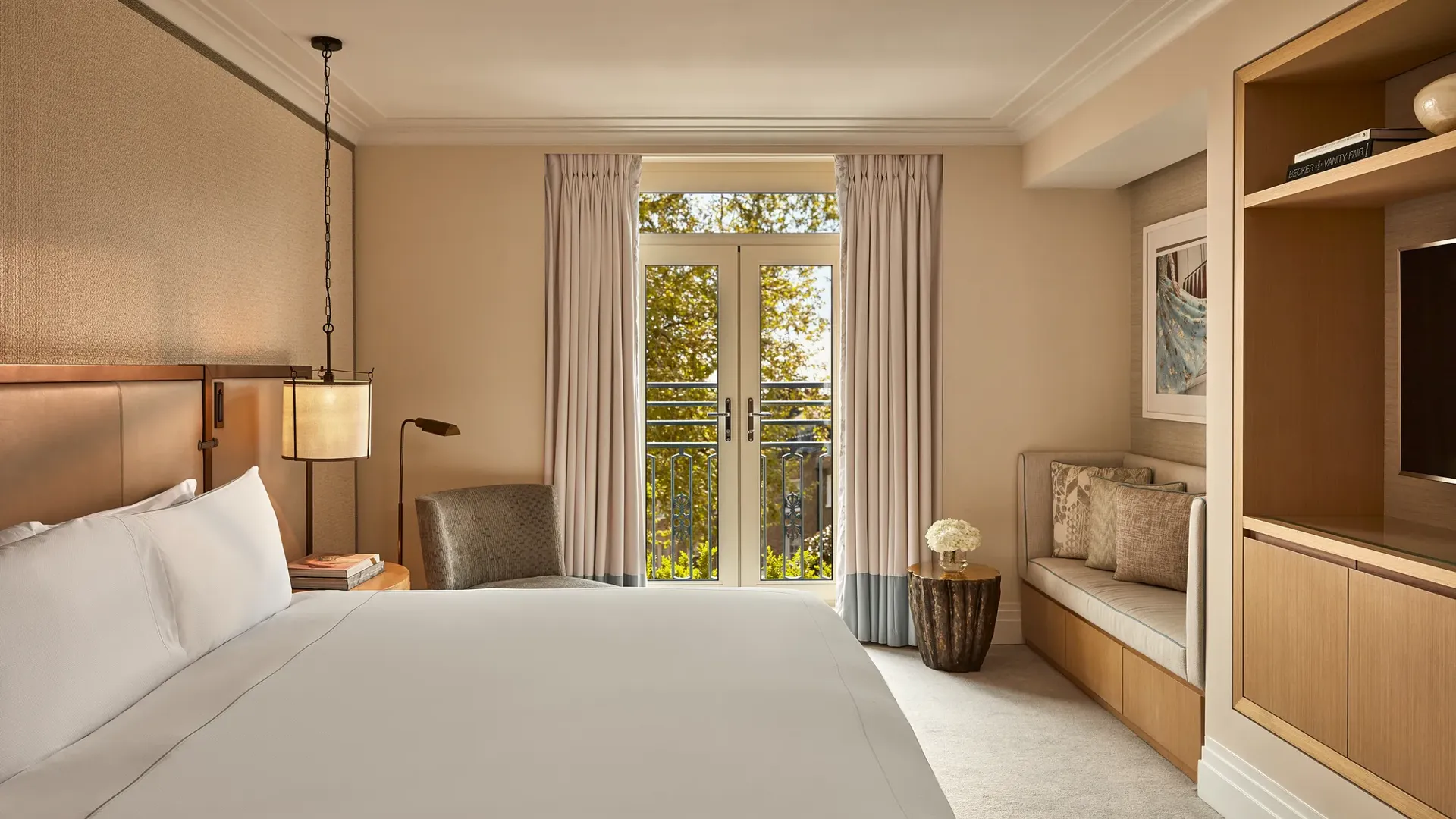 Hotel room with king bed, soft neutral tones, French doors to balcony, and seating area.
